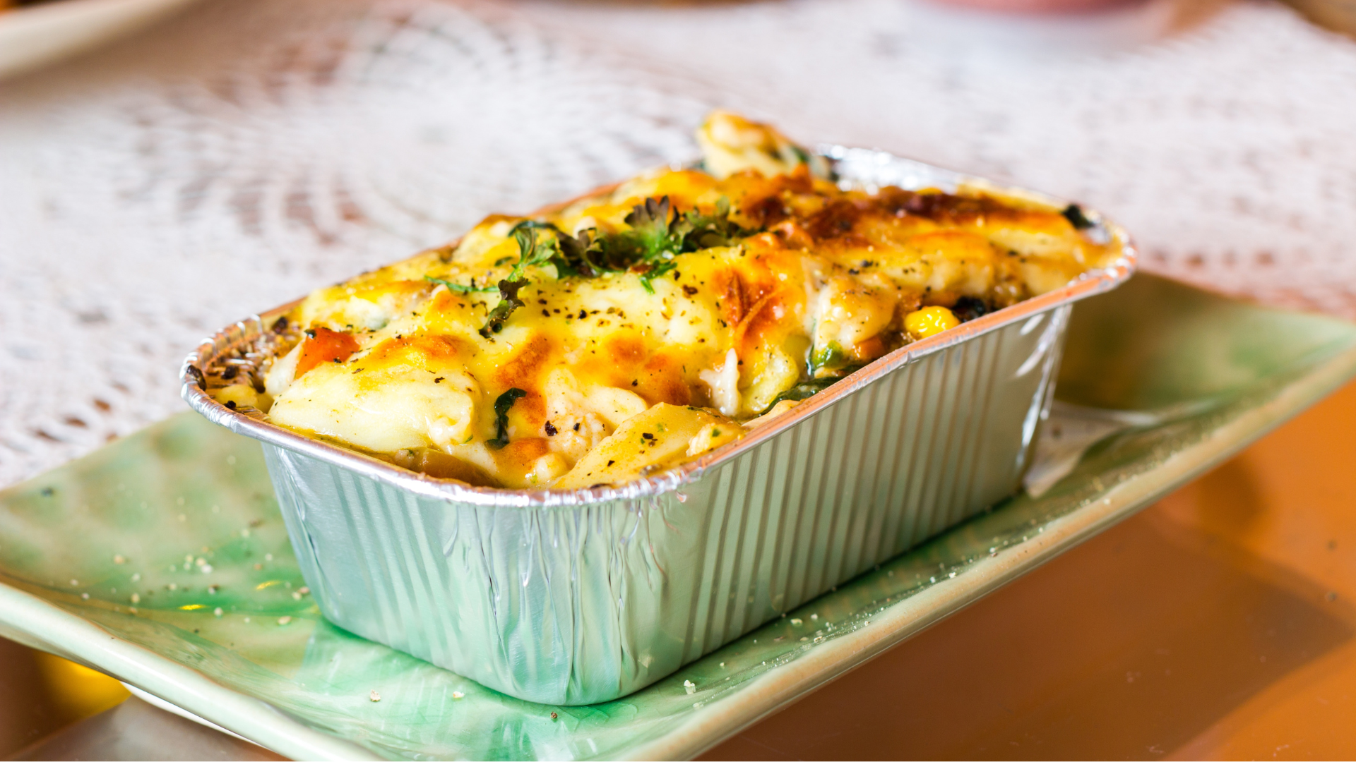 Lasagne ready meal in a foil container on a plate, on a table.