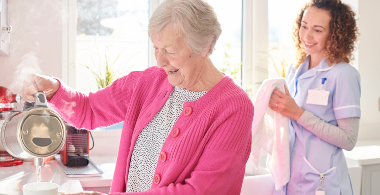 A carer helping an older woman make a hot drink in her home.