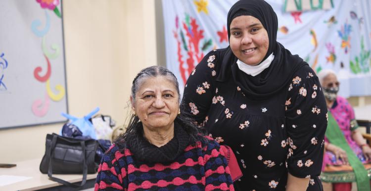A woman wearing a headscarf providing medical care to an older Asian woman.