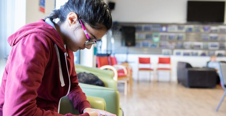 A young woman sitting in a communal room looking at her phone