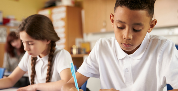 Two children writing on pieces of paper in a primary school classroom