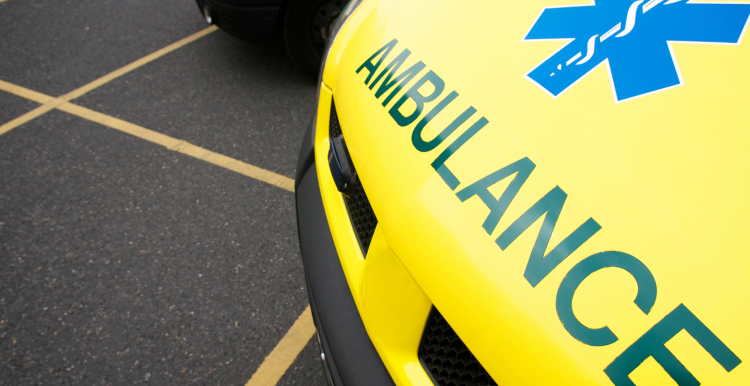 The front of a yellow ambulance, parked in a car park.