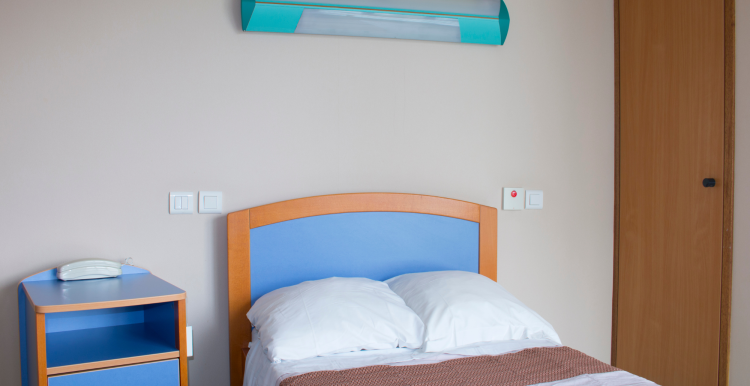 A hospital ward bedroom with a single bed, cupboard, and bedside table