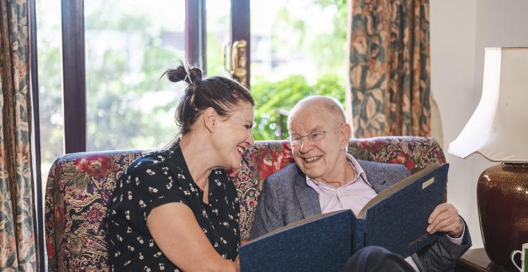 A woman and older man sitting on a sofa, looking at a photo album