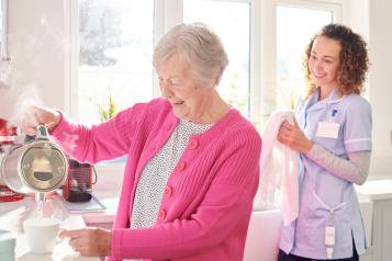 A carer helping an older woman make a hot drink in her home.