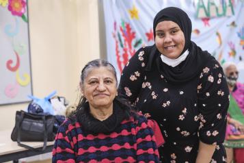 A woman wearing a headscarf providing medical care to an older Asian woman.