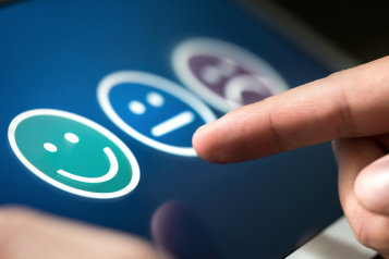 A screen showing a smiling face, a neutral face, and a sad face. A person is selecting one of the faces.