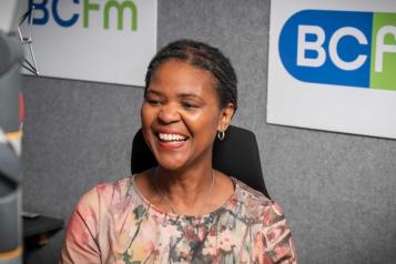 A woman smiling, sitting behind a microphone.