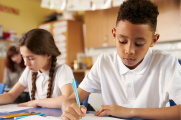 Two children writing on pieces of paper in a primary school classroom