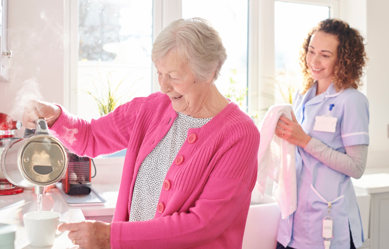 A carer helping an older woman make a hot drink in her home.