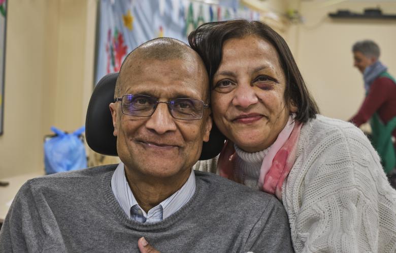 An older couple hugging and smiling. The man is in a wheelchair or powerchair.