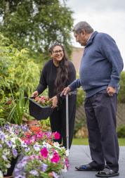 An older man using a walking stick and a younger woman gardening.